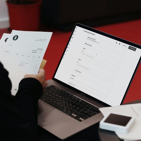 Persona salīdzina papīra rēķinu ar portatīvā datora ekrānā atvērtu programmu.